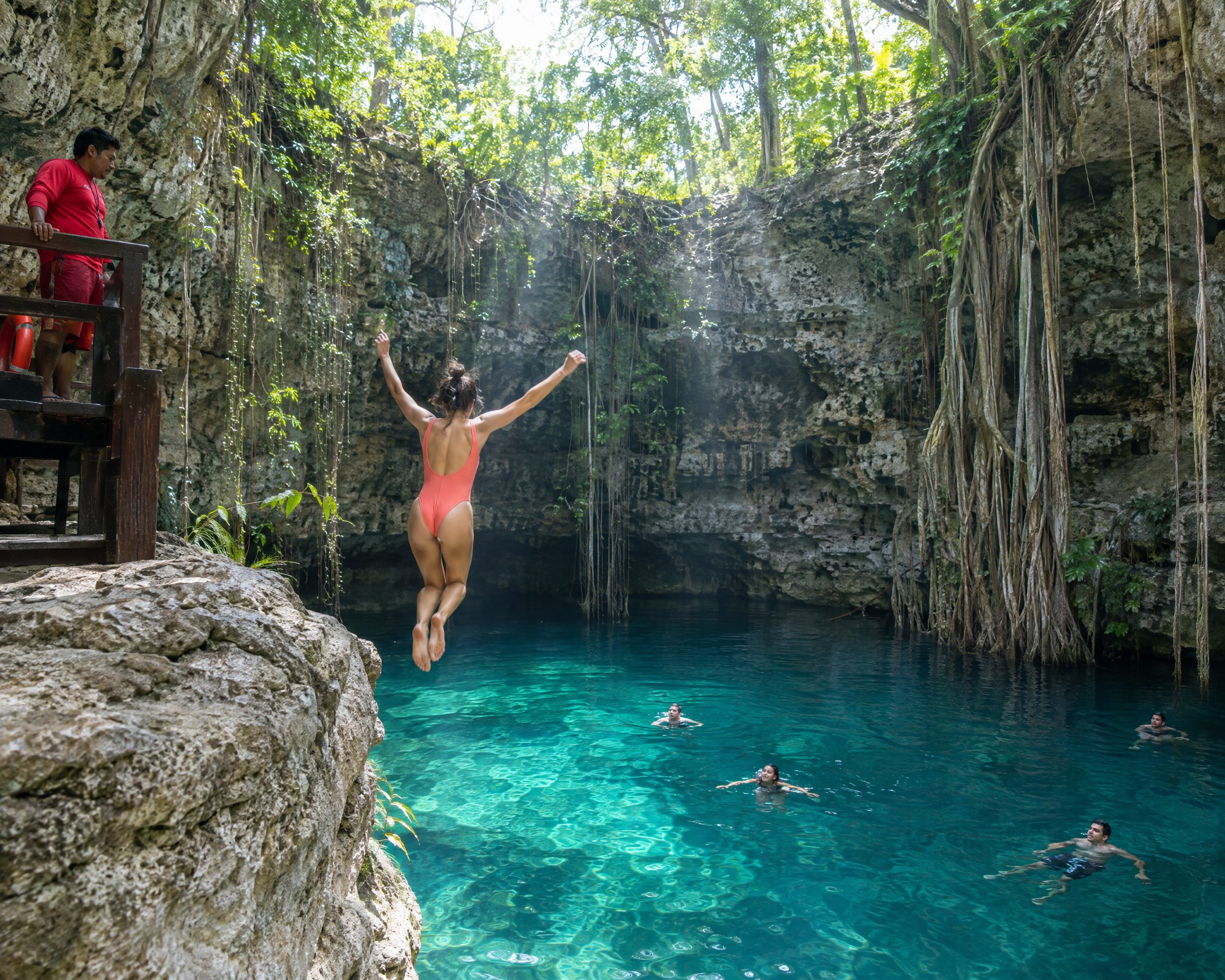 A swimmer jumps from a limestone ledge into a turquoise cenote